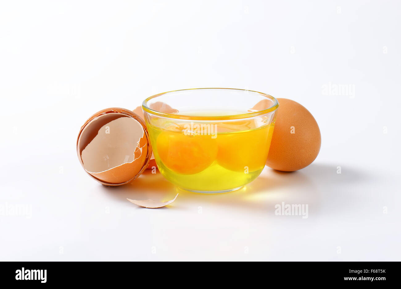 Frisches Eiweiß und Eigelb in Glasschale, ein ganzes Ei und leeren Eierschalen Stockfoto