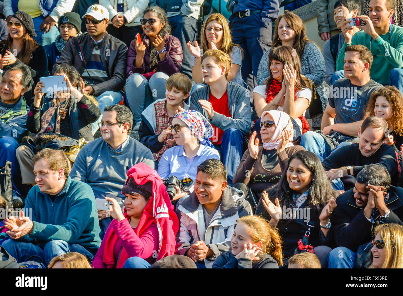 Eine große, vielfältige Gruppe von multi-ethnischen Menschen draußen sitzen in Reihen als Zuschauer Künstler auf der Straße, beim Klatschen mit fröhlichen Antworten Stockfoto