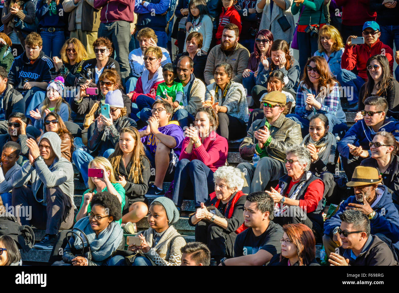 Eine große, vielfältige Gruppe von Menschen, die draußen sitzen in Reihen als Publikum gerade eine live-Performance und fröhlich reagiert Stockfoto