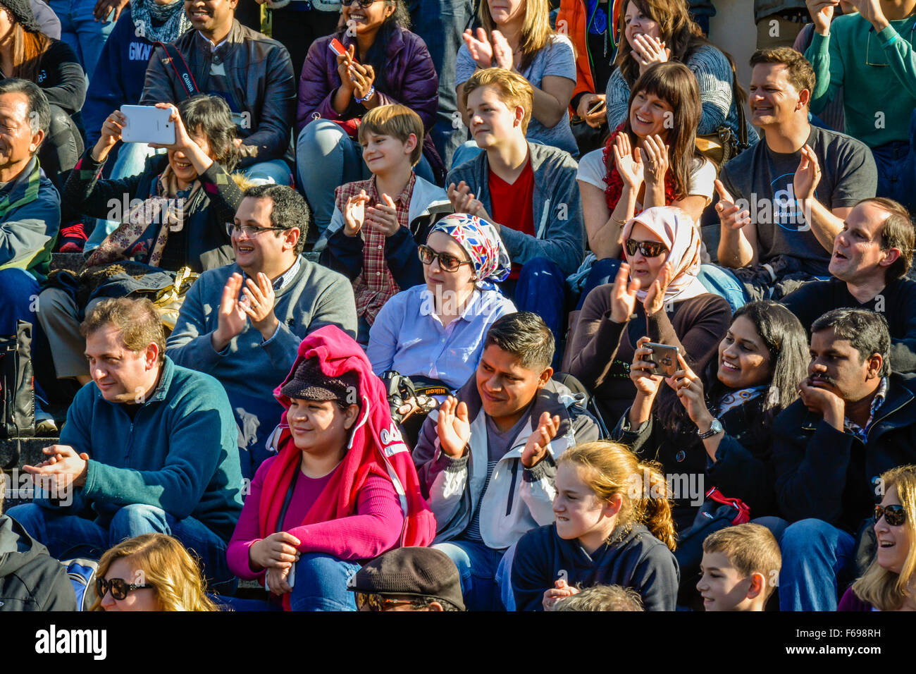 Eine große, vielfältige Gruppe von Menschen, die draußen sitzen in Reihen als Publikum gerade eine live-Performance und fröhlich reagiert Stockfoto