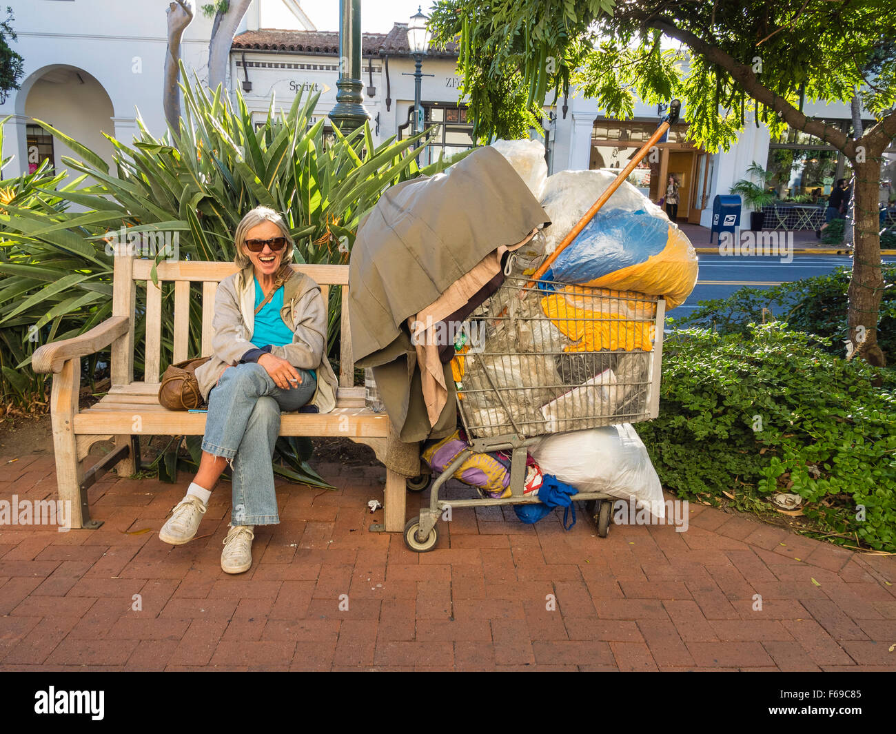 Eine Seniorin Stadtstreicherin Sonnenbrille lacht als sie auf einer öffentlichen Bank auf der State Street, eine Zigarette rauchend sitzt. Stockfoto