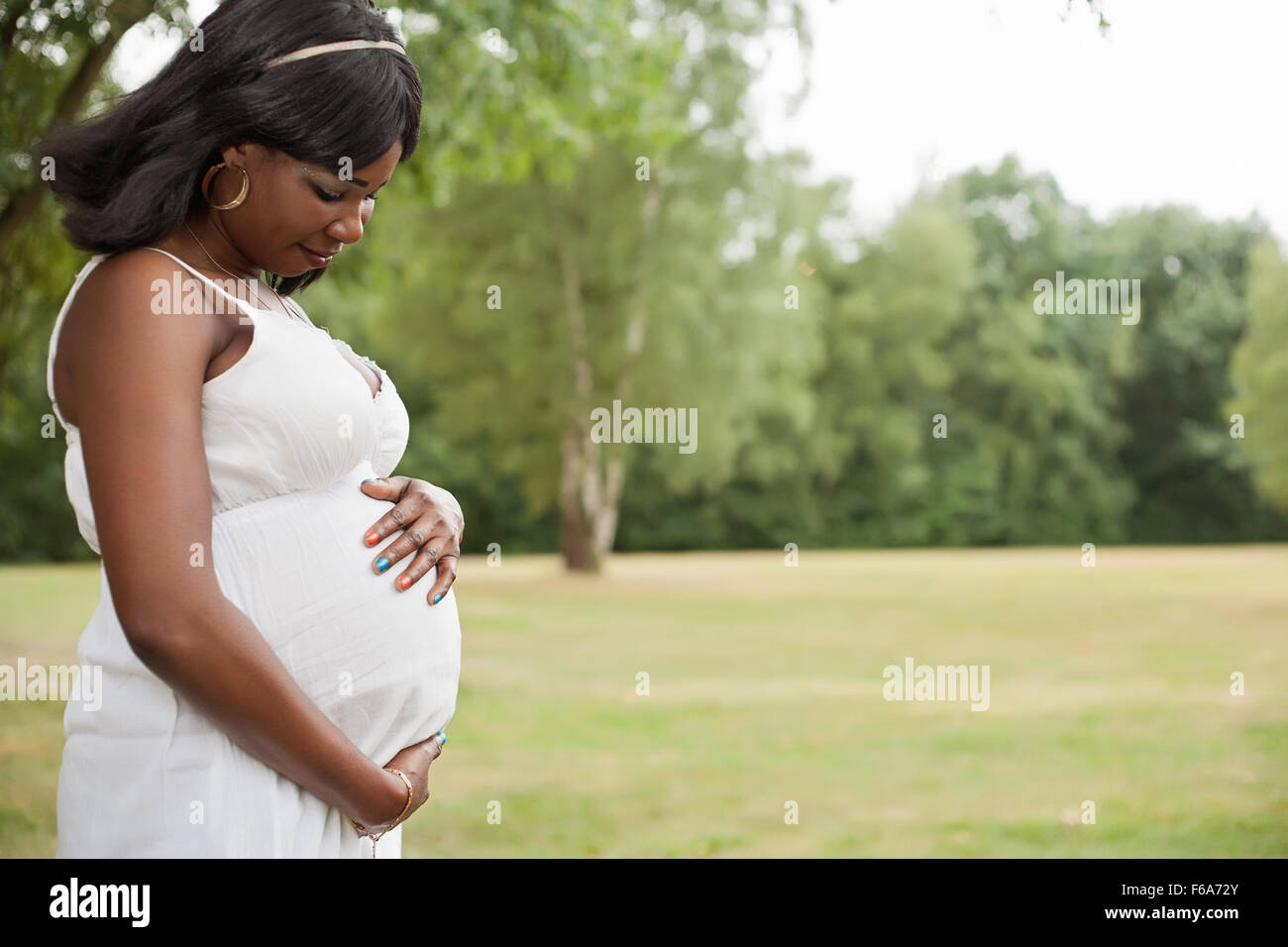 Schwangere Afrikanerin in der Natur mit weißen Kleid Stockfoto