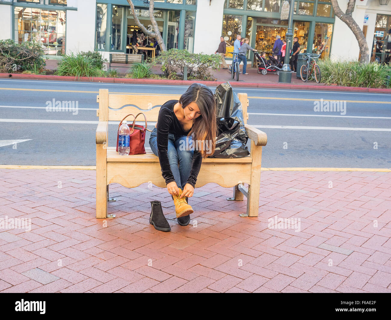 Eine junge Hispanic Frau verwandelt sich in die neuen Schuhe, die sie gerade auf einer öffentlichen Bank auf dem Bürgersteig auf der State Street in gekauft Stockfoto