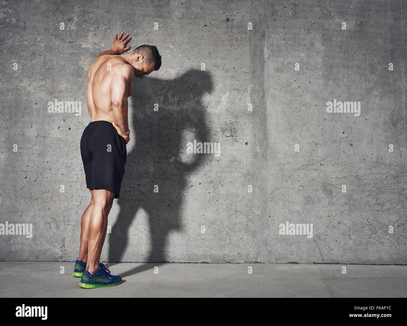 Junger Mann, ruhen Sie sich nach einer aktiven Fitnesstraining stehend gegen graue Wand mit Kopie-Space-Bereich für Ihre SMS-Nachricht, Stockfoto