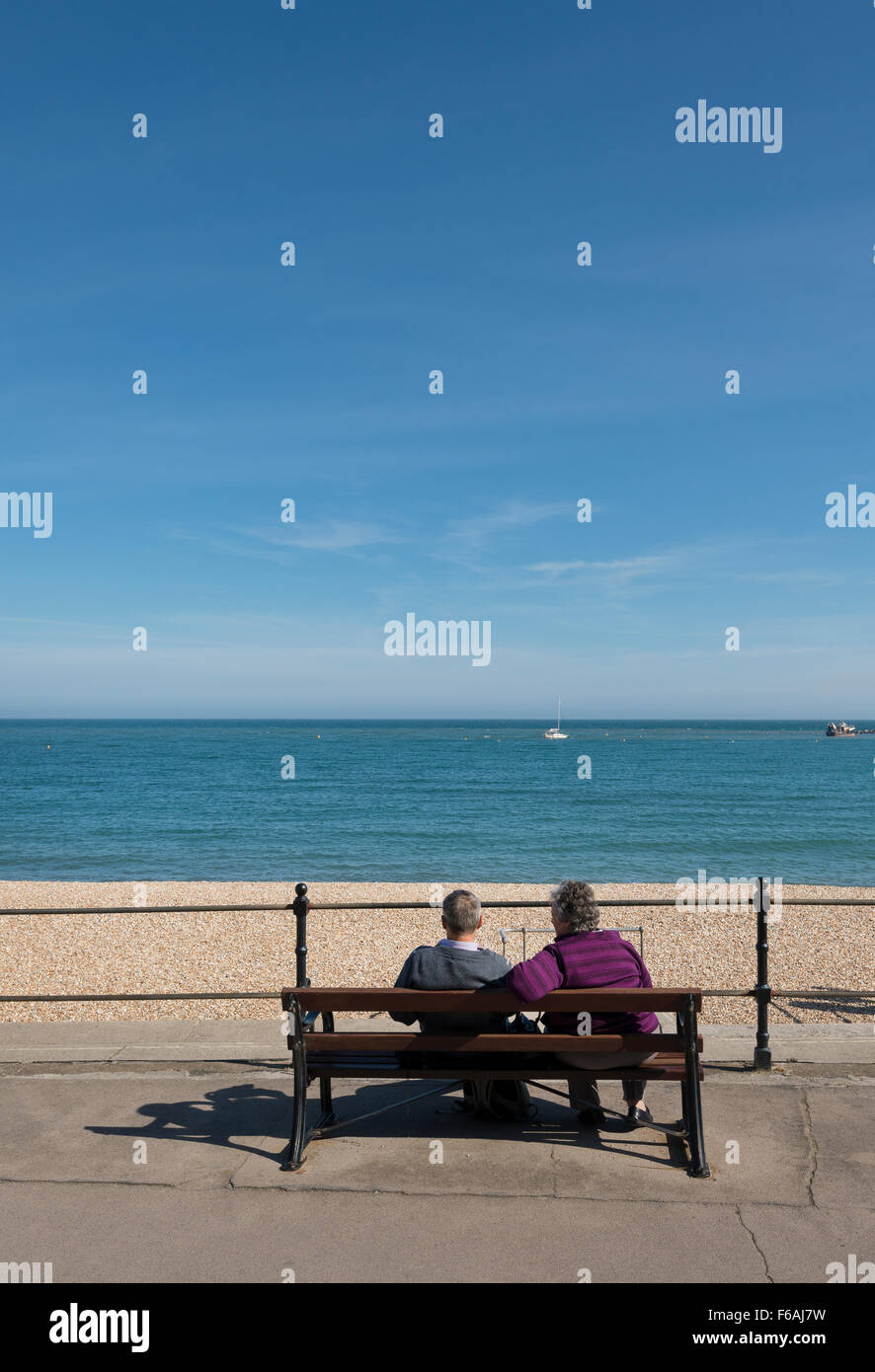 Mittleren gealterten paar sitzt auf Holzbank auf Lyme Regis direkt am Meer mit Blick auf das Meer Stockfoto