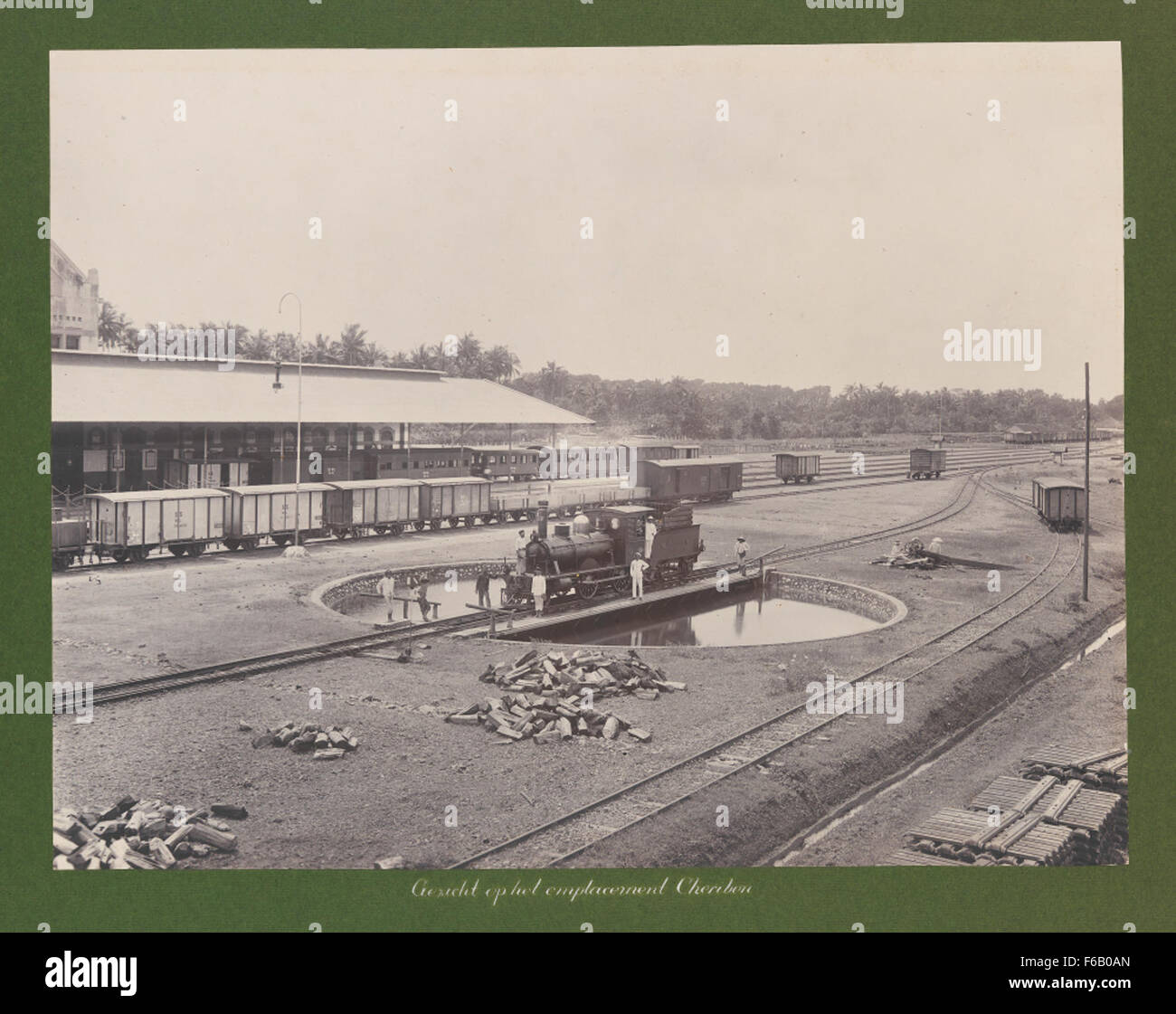 Dieses historische Kunstwerk zeigt den Bahnhof Cheribon und seine staatlichen Depots, Lokomotiven und Eisenbahninfrastruktur. Die Szene fängt die industrielle Stärke und Größe des Transportsystems im frühen 20. Jahrhundert ein. Stockfoto