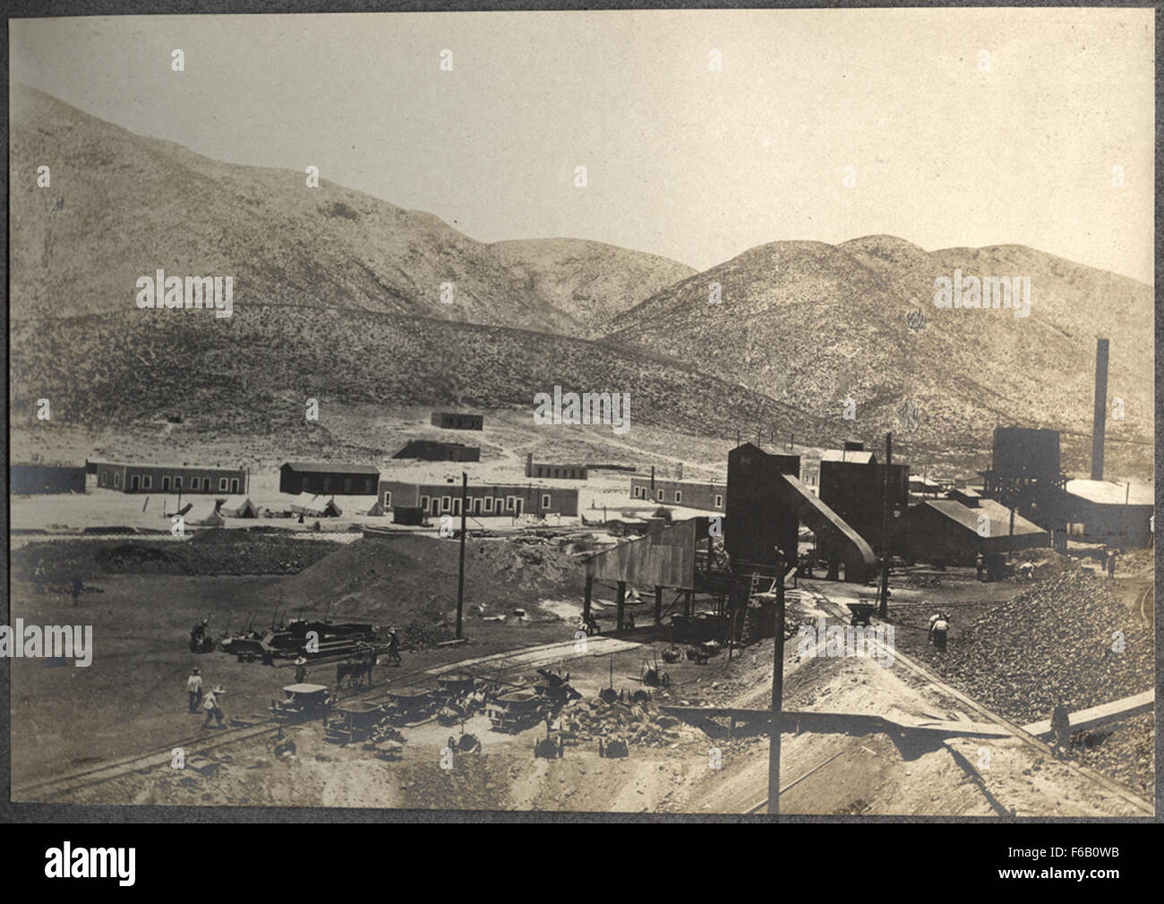Diese Industrieszene zeigt eine Hütte und Schlackenhalde mit Bergbaugebäuden und Männern im Hintergrund, die die harten Bedingungen der frühen Bergbaubetriebe veranschaulichen. Stockfoto
