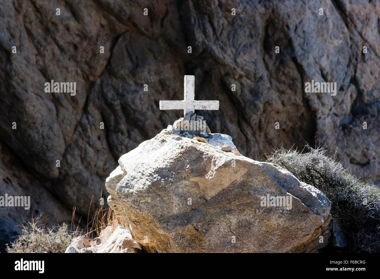 Santorini. Christian Kreuz, erleuchtet von starker Sonneneinstrahlung in Haufen von Steinen auf Rock mit Hintergrund der dunklen Felsen im Schatten gepflanzt. Stockfoto