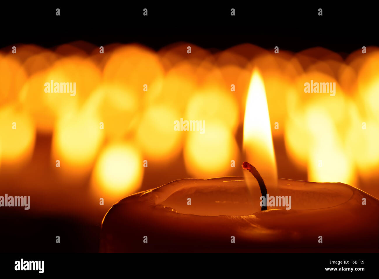 Kerze vor vielen defokussierten Candleflames schafft eine spirituelle Atmosphäre und im Gedenken an Ihren lieben Stockfoto