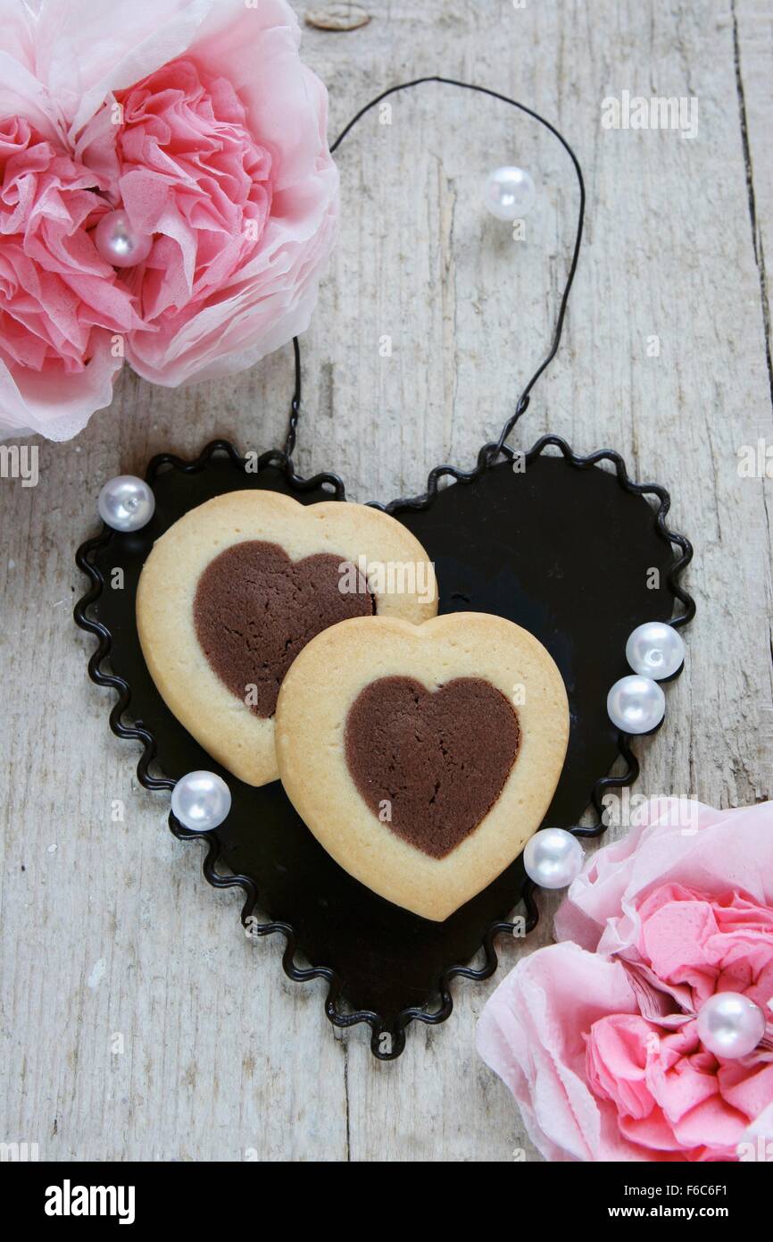 Zweifarbige herzförmige Kekse auf ein schwarzes Metall Herz zwischen Papier Nelken Stockfoto