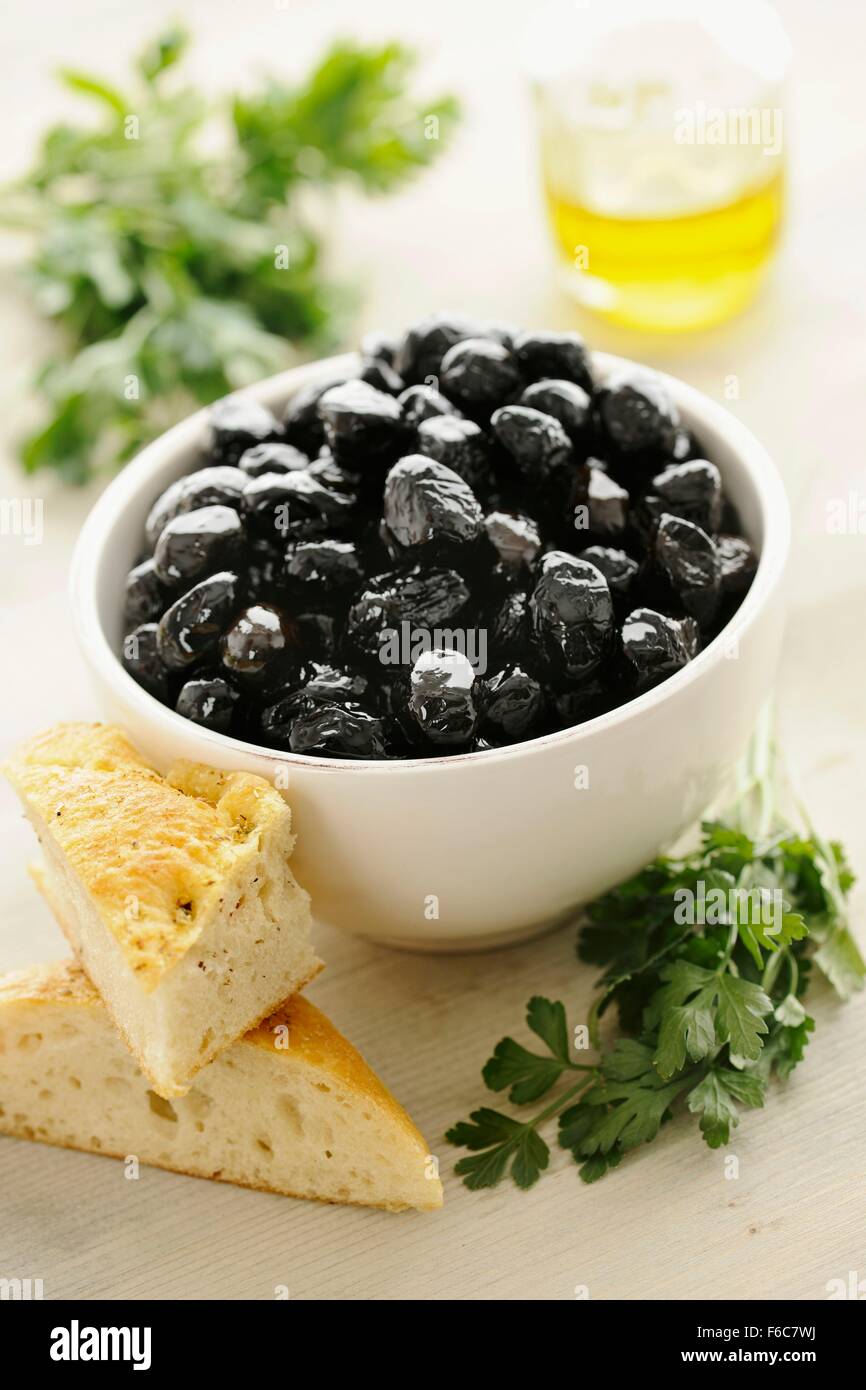 Schwarze Oliven in eine Schüssel geben, mit Brot und Petersilie Stockfoto