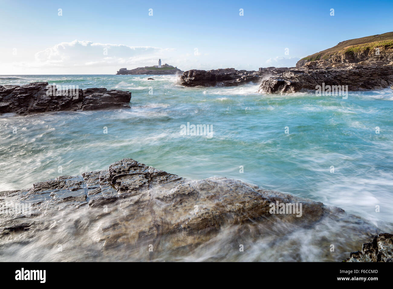 Wellen über die Felsen bei Godrevy Point, Blick auf den Leuchtturm auf der Insel Godrevy, Cornwall, England Stockfoto