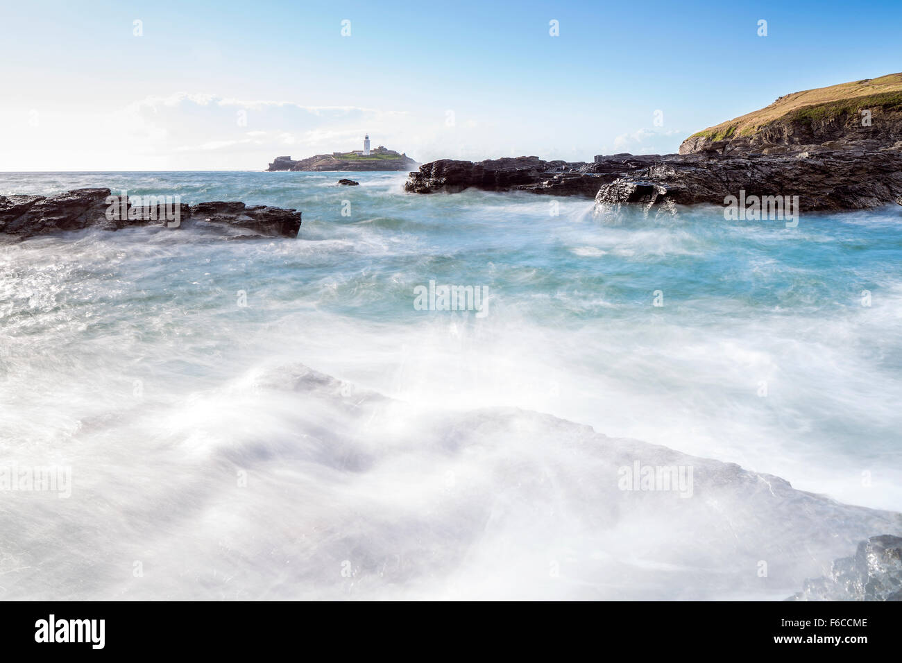 Wellen über die Felsen bei Godrevy Point, Blick auf den Leuchtturm auf der Insel Godrevy, Cornwall, England Stockfoto