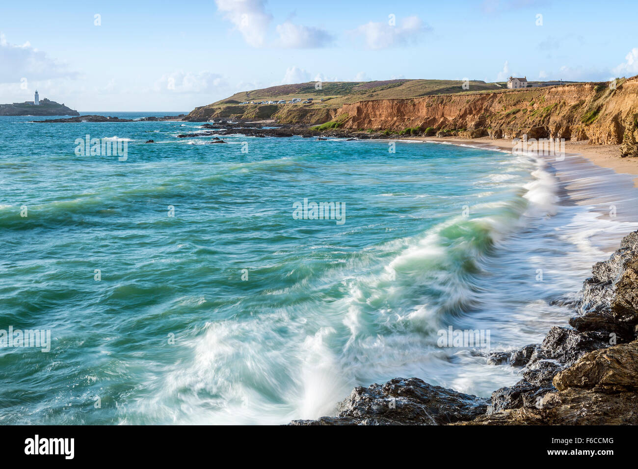 Wellen über die Felsen bei Godrevy Point, Blick auf den Leuchtturm auf der Insel Godrevy, Cornwall, England Stockfoto