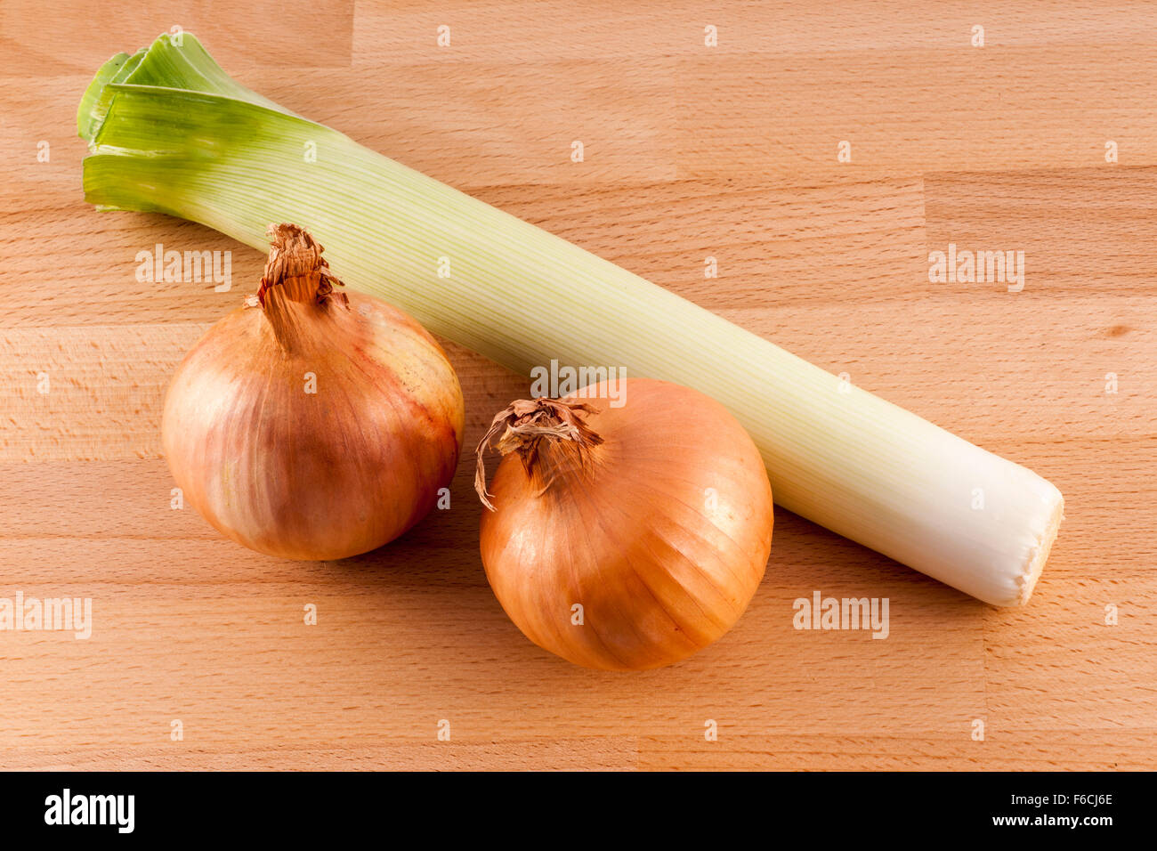 Zwei frische Zwiebeln und Lauch auf einem Holzbrett-Hintergrund Stockfoto