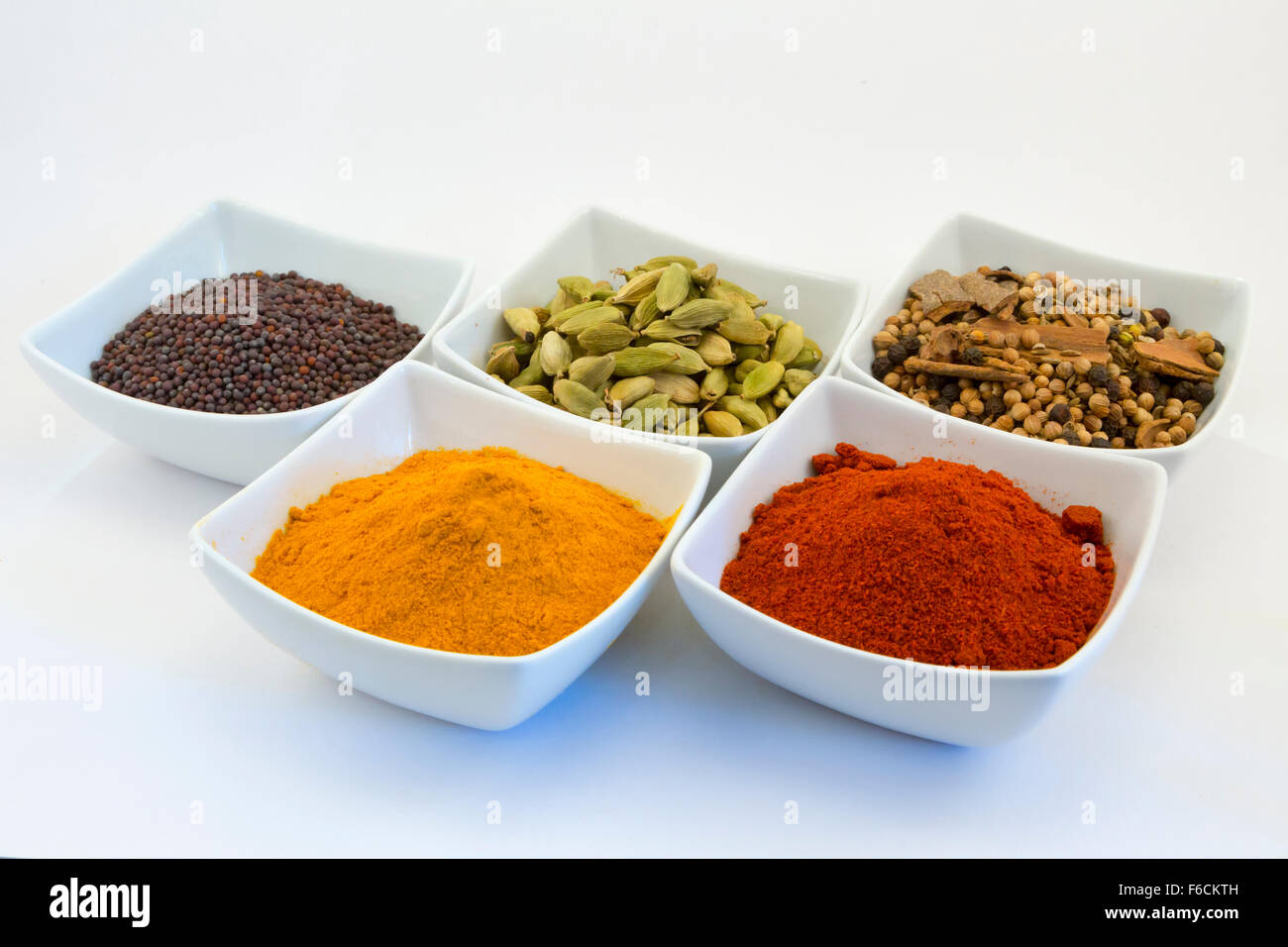 Eine Auswahl an Curry-Gewürze (Senf, Cardomom, Garam Masala, Kurkuma, Paprika) in Schalen vor einem weißen Hintergrund Stockfoto