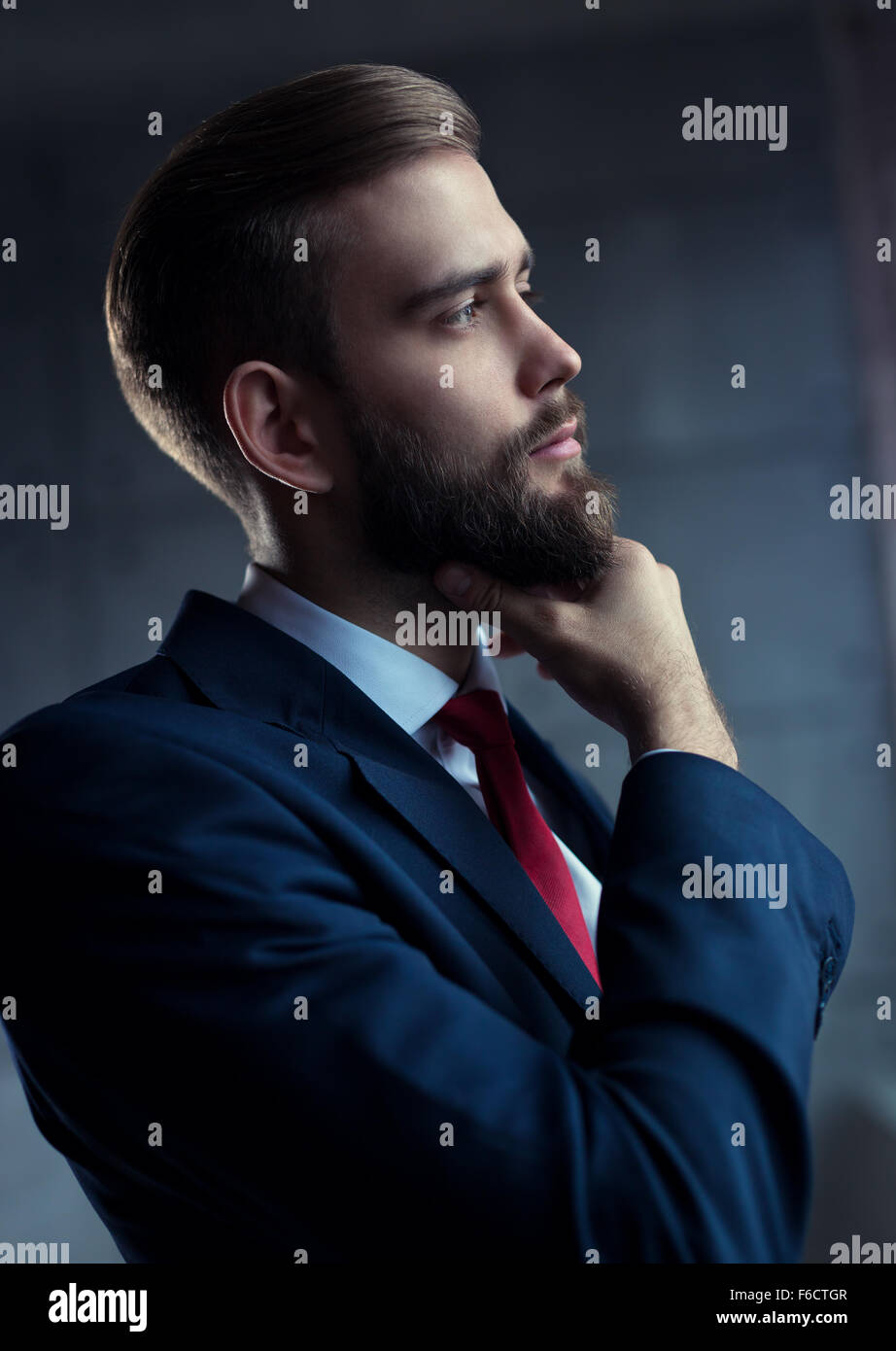 Schönen jungen Mann mit Bart im schwarzen Anzug in nachdenklicher Pose nach draußen zum Fenster. Stockfoto