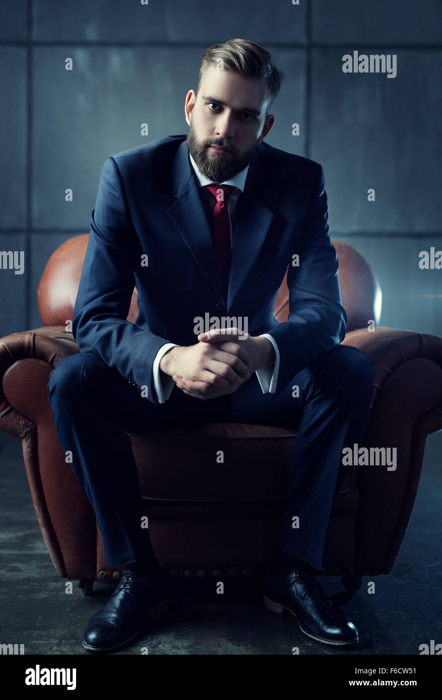 Junge hübscher Geschäftsmann mit Bart in schwarz passen auf Stuhl sitzend und Lautsprecher aufmerksam zuhört. Stockfoto