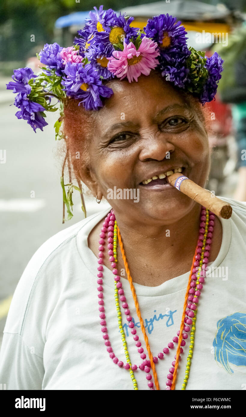 alten kubanischen mit Blumenschmuck im Haar Rauchen einer Zigarre und Post für den Fotografen, La Habana, Havana, La Habana, Straße Stockfoto