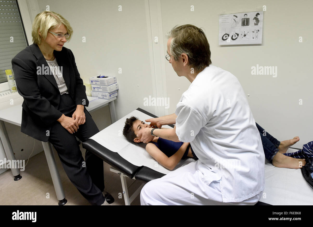 Schleswig-Holstein-Minister für Gesundheit und Soziales, Kristin Alheit (SPD, L), schaut zu, wie Kinderarzt Professor Werner Nikischin (R) acht - jährige Mustafa (C) aus Syrien in der Empfangsstelle Flüchtling in Neumünster, Deutschland, 17. November 2015 untersucht. Mit der verbesserten Charakters der medizinische Behandlung für Flüchtlinge war Alheit Aufholjagd. Die Universität Krankenhaus des Landes Schleswig-Holstein (UKSH) eingerichtet, Container, Zelte und eine x-ray Scanner Station medizinische Untersuchungen, Behandlung und Betreuung der Flüchtlinge in Schleswig-Holstein größte Empfangsstelle, die vor kurzem beherbergen Stockfoto