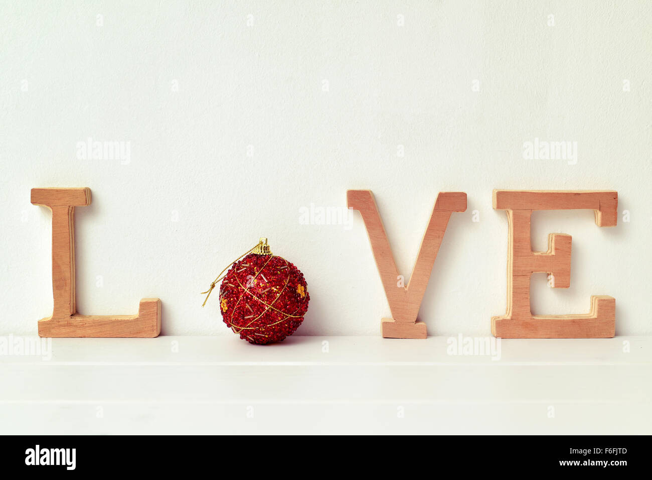 einige Holzbuchstaben und eine rote Weihnachtskugel bilden das Wort Liebe auf eine weiße Szene Stockfoto