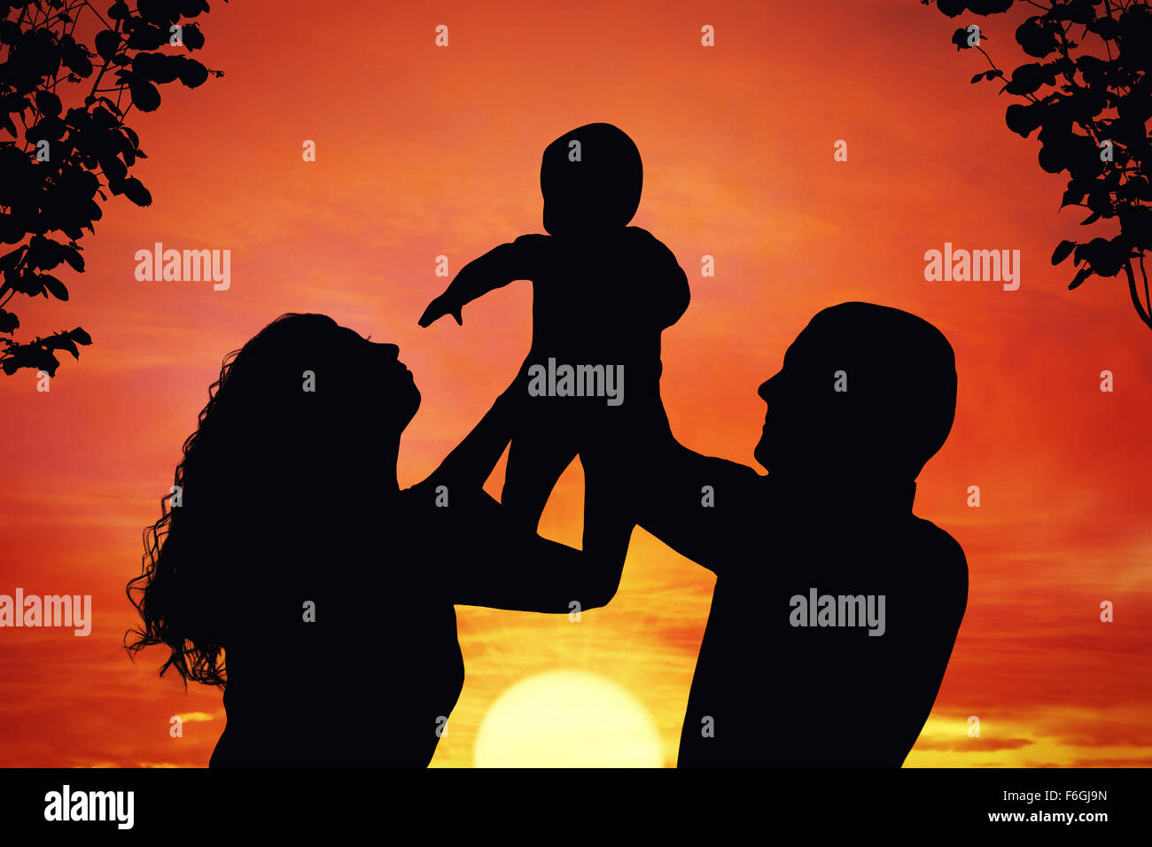 Eltern mit ihrem kleinen Kind bei Sonnenuntergang, Baby in die Luft hob. Silhouette einer glücklichen Familie von drei Personen Stockfoto