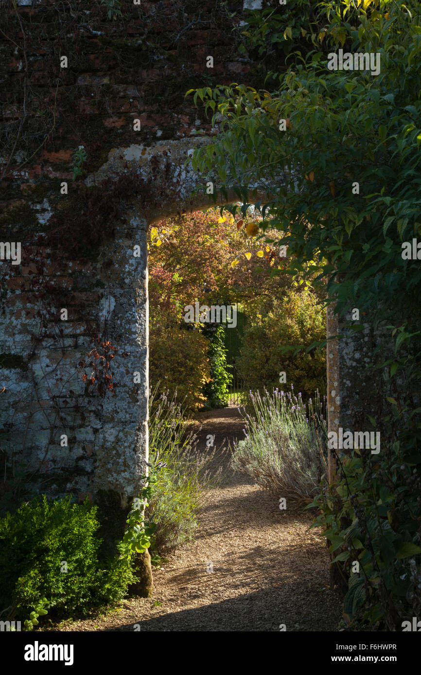 Ein Cotswold-Torbogen aus Stein, der in einer hohen Backsteinmauer mit warmer Oktobersonne aufgestellt ist, Rousham House Gardens, Oxfordshire, England. Stockfoto