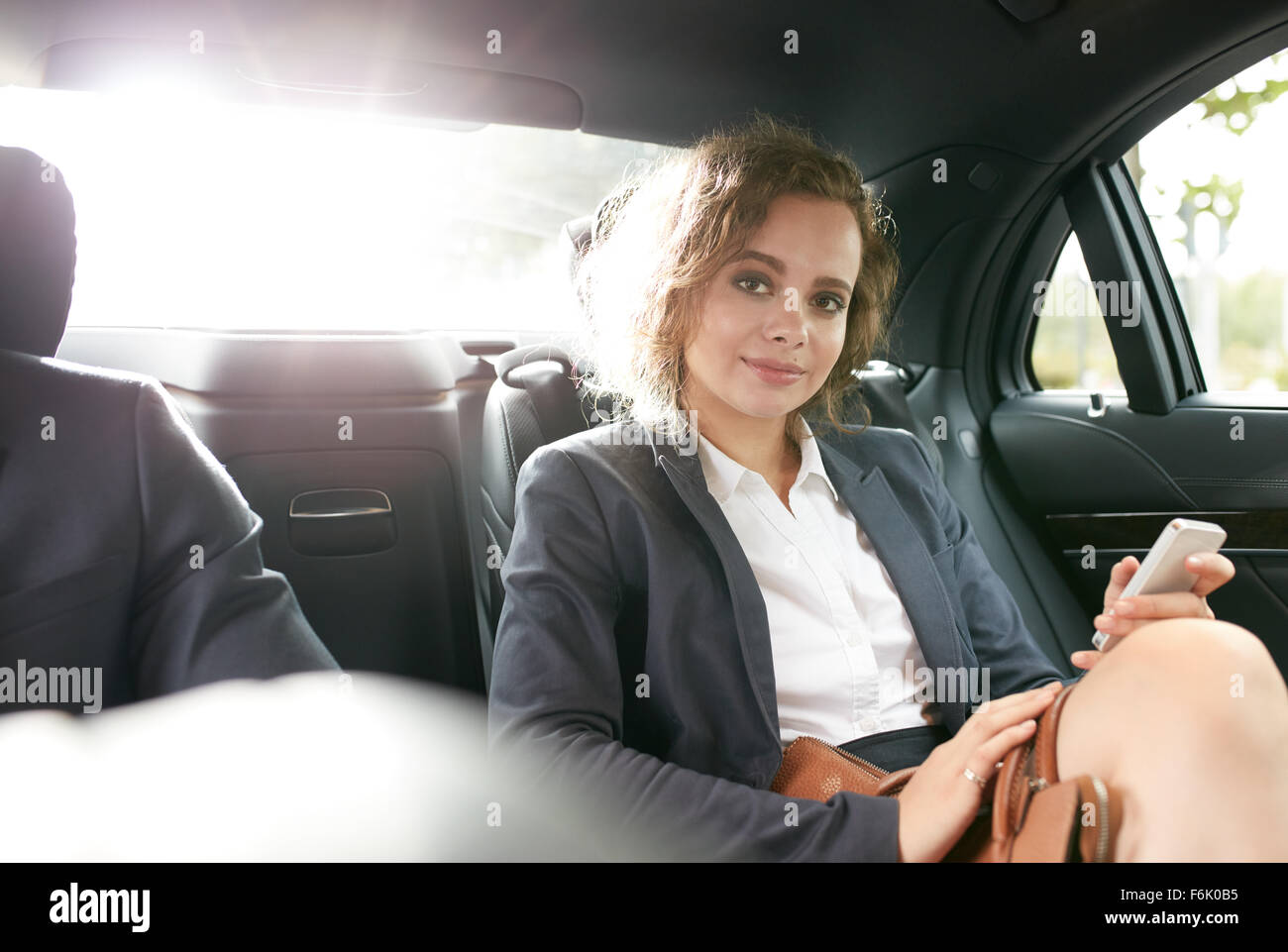 Porträt von zuversichtlich Geschäftsfrau im Rücksitz eines Autos mit ihrem Handy in der hand Blick in die Kamera. Stockfoto