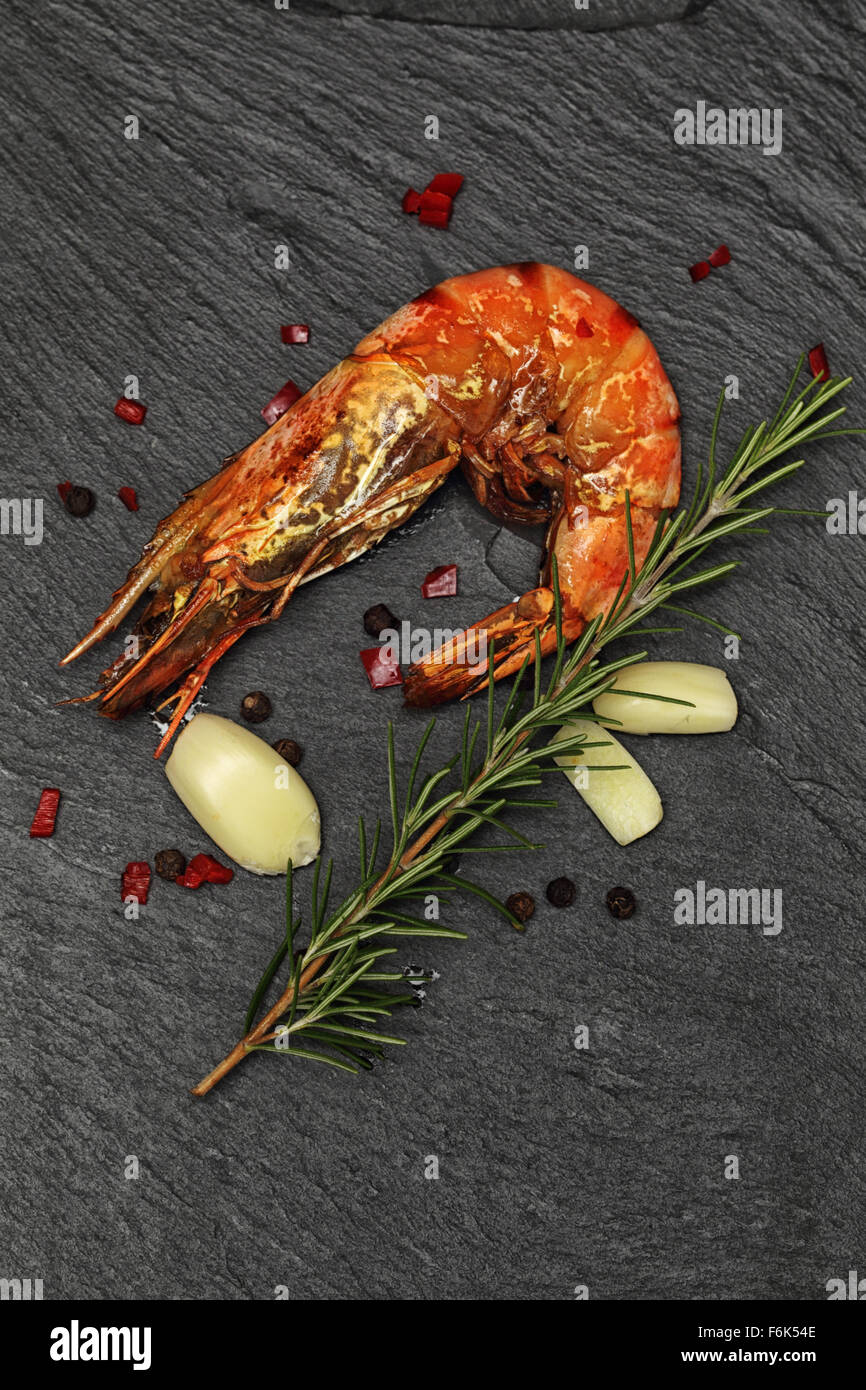 Gegrillte ganze Riesen Garnelen mit Rosmarin, Knoblauch und rotem Chili auf schwarzem Schiefer Hintergrund. Stockfoto