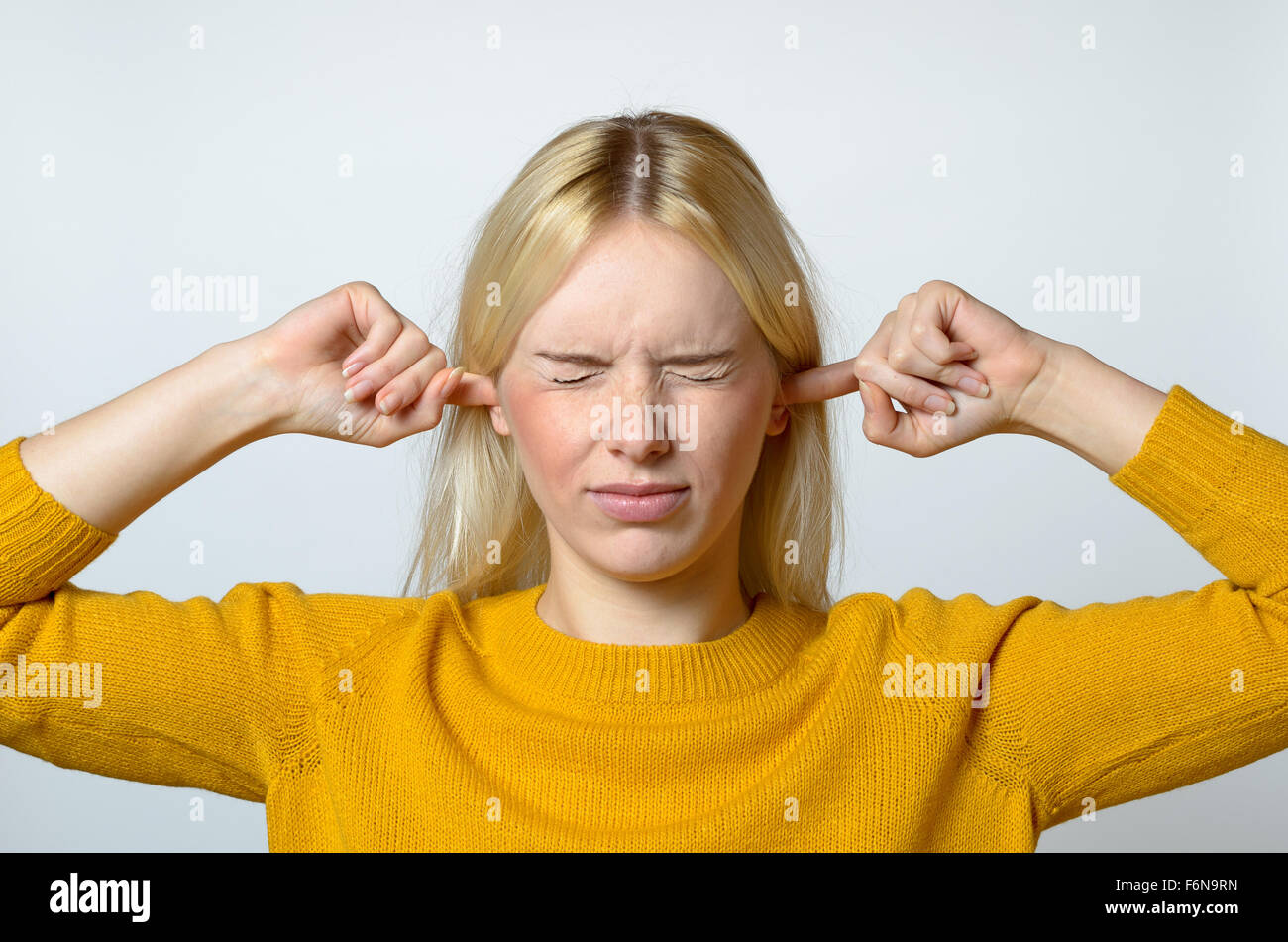 Nahaufnahme angewidert junge Frau deckt ihre Ohren mit den Fingern, mit geschlossenen Augen, gegen grauen Hintergrund. Stockfoto