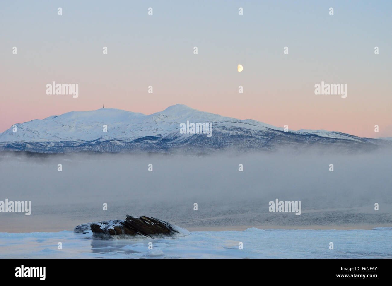 Eis-Nebel und Dunst über Fjord mit farbenfrohen Sonnenaufgang Himmel hinter mächtigen Schneeberg Stockfoto