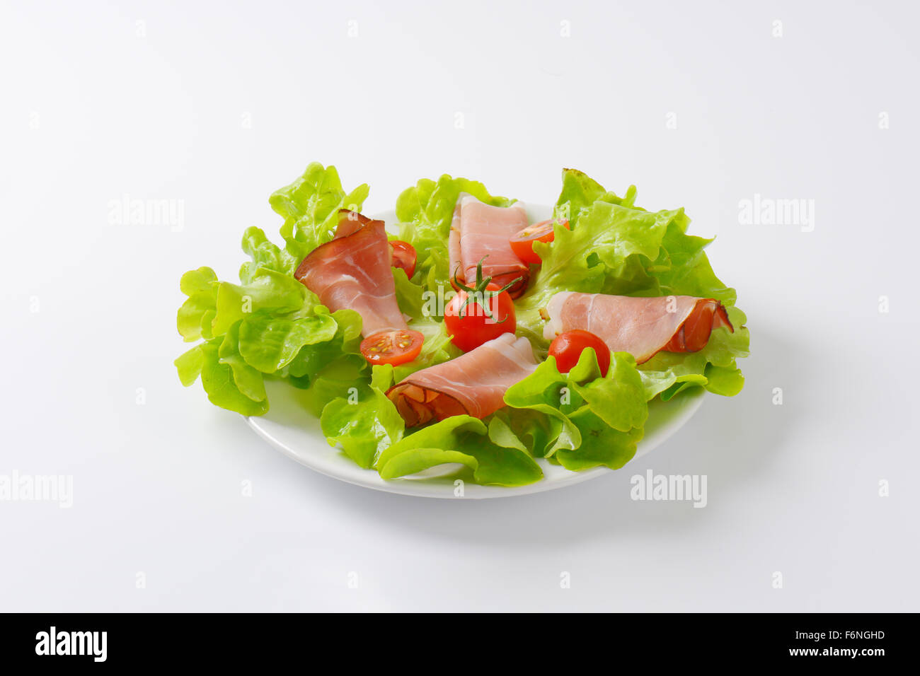 Teller mit frischem Salat und getrockneter Schweineschinken auf weißem Hintergrund Stockfoto