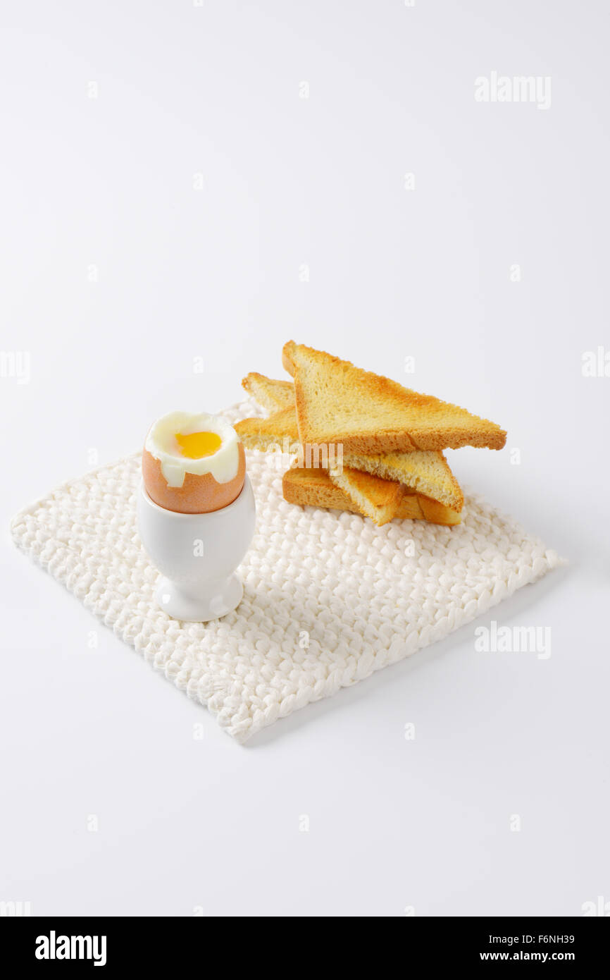 weich gekochtes Ei im Eierbecher und knusprige Toasts auf weißen Untersetzer Stockfoto
