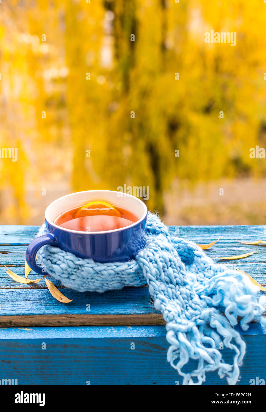 Tasse Tee mit Schal auf blauen Holztisch, verschwommene herbstlichen Sonnenuntergang auf Hintergrund Stockfoto