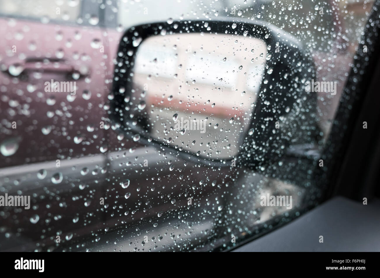 Nassen Sie Autofenster mit Regentropfen und einen Spiegel hinter. Nahaufnahme Foto mit Tiefenschärfe und flachen DOF Stockfoto