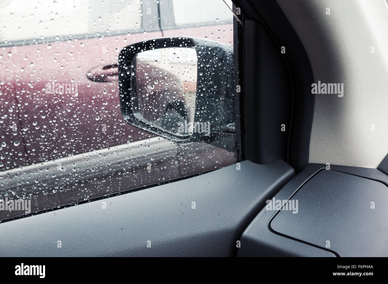 Nassen Sie Autofenster mit Regentropfen und einen Spiegel hinter. Nahaufnahme Foto mit Tiefenschärfe und flachen DOF Stockfoto