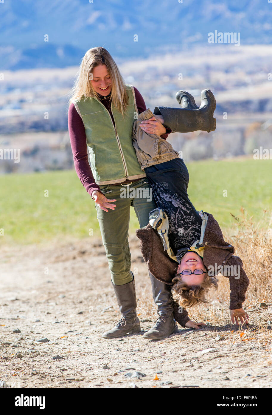 Attraktive Mutter spielerisch mit ihrem kleinen Sohn auf dem Kopf stehend auf Schmutz Weg auf ranch Stockfoto