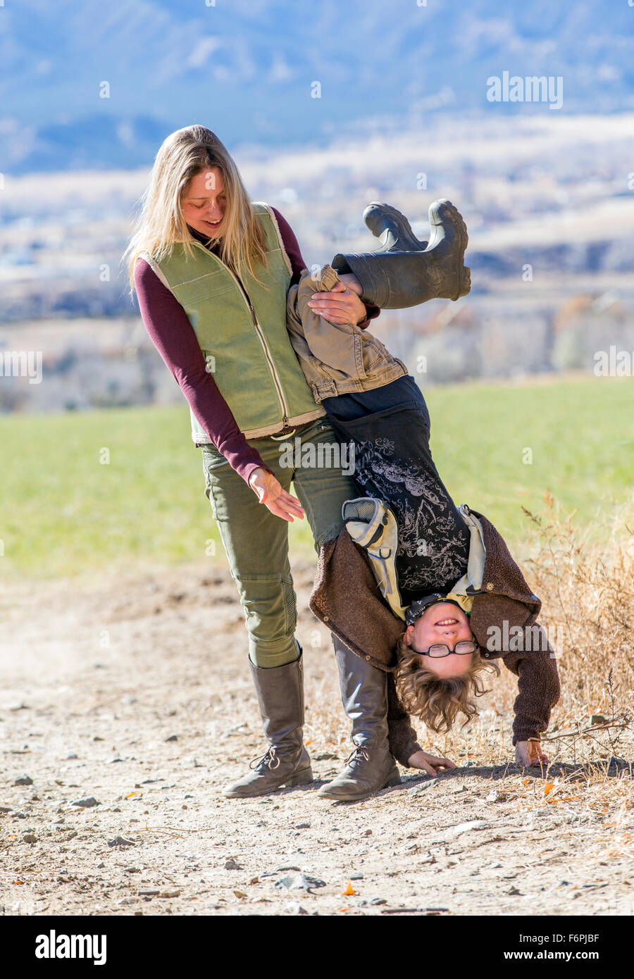 Attraktive Mutter spielerisch mit ihrem kleinen Sohn auf dem Kopf stehend auf Schmutz Weg auf ranch Stockfoto