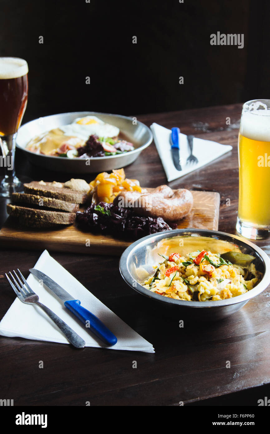 Schüssel mit Nudeln, Käse auf Schneidebrett und Bier am Tisch Stockfoto
