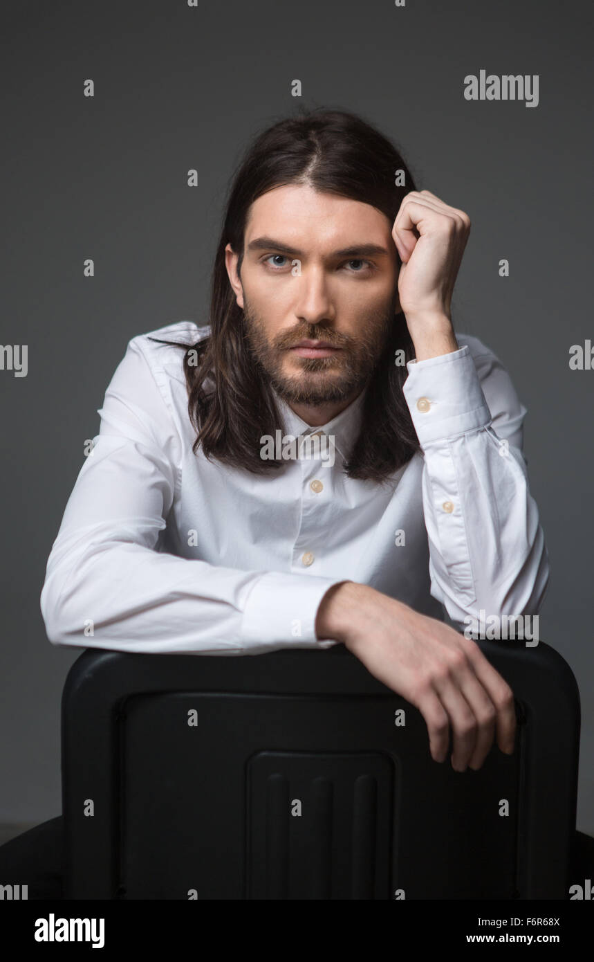 Junger Mann mit Bart und langen Haaren, Blick in die Kamera über Hintergrund Stockfoto