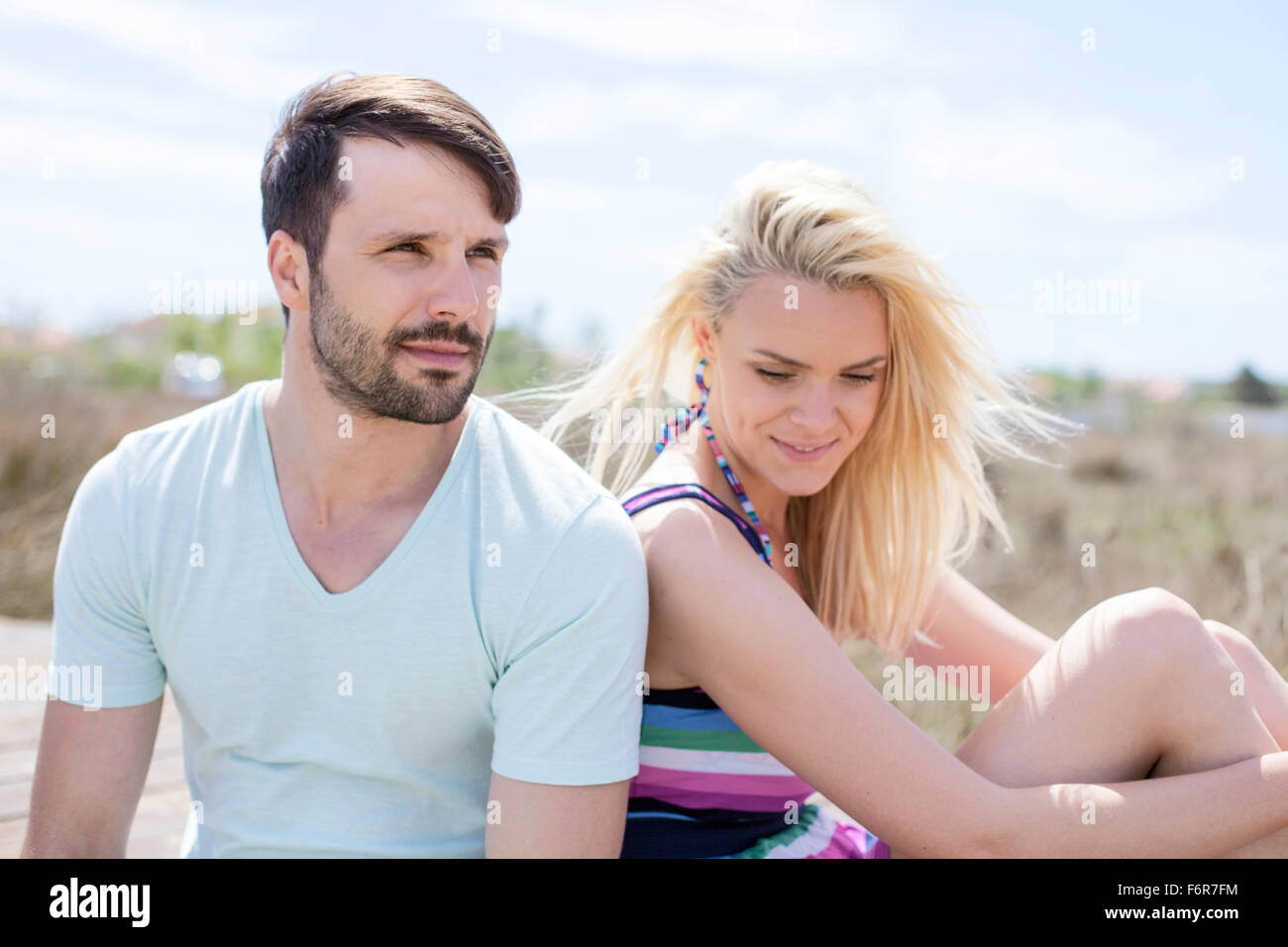 Junges Paar sitzen nebeneinander am Strand Stockfoto