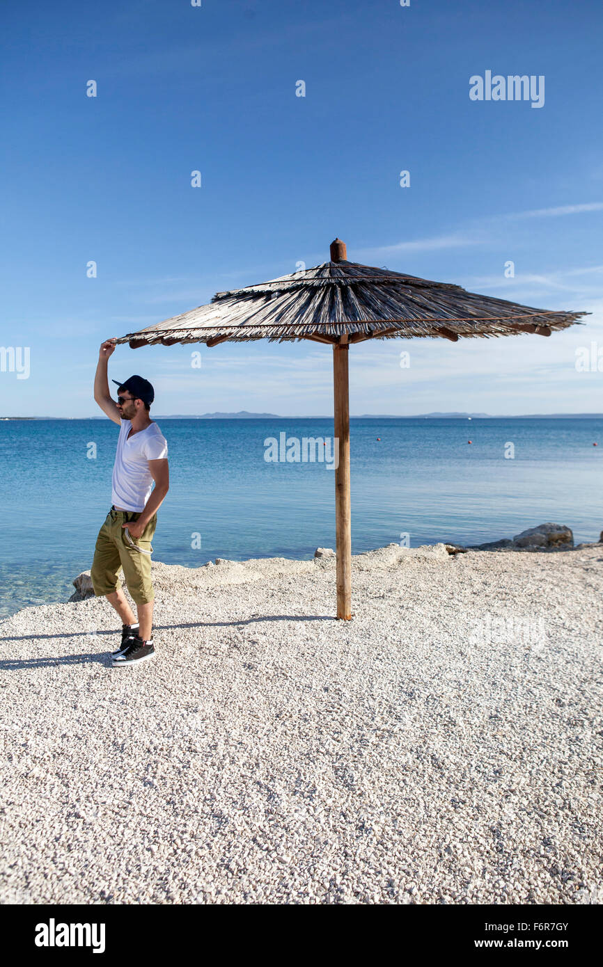 Junger Mann stehend unter Sonnenschirm am Strand Stockfoto