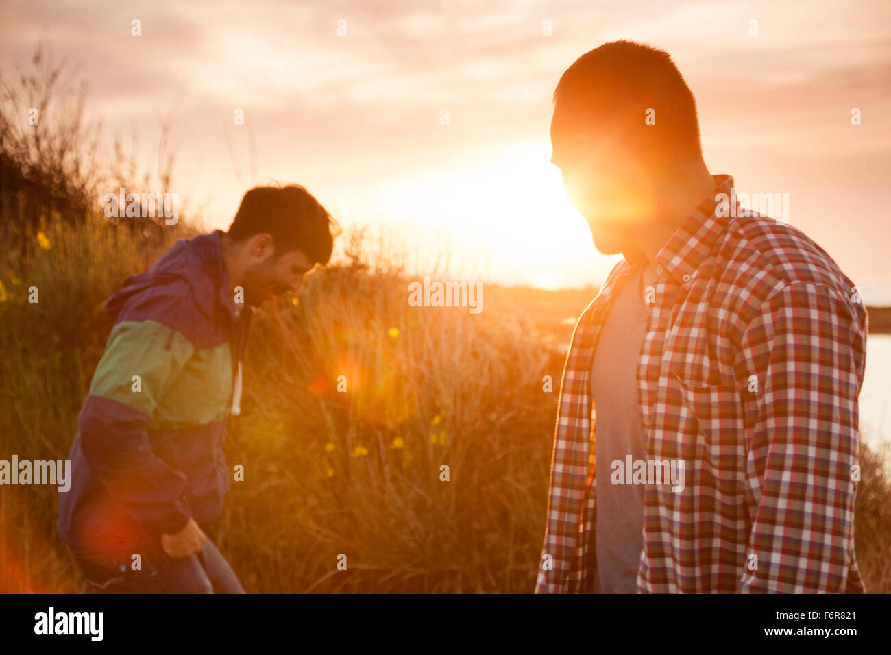 Zwei Freunde am Rand des Wassers sprechen bei Sonnenuntergang Stockfoto