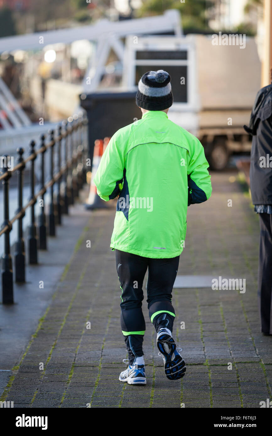 Ein älterer Mann trägt eine wollige Pudelmütze, läuft Trainingsanzug Hose und einem grünen hi-viz Spitze weg von der Kamera auf die Docks in Stockfoto