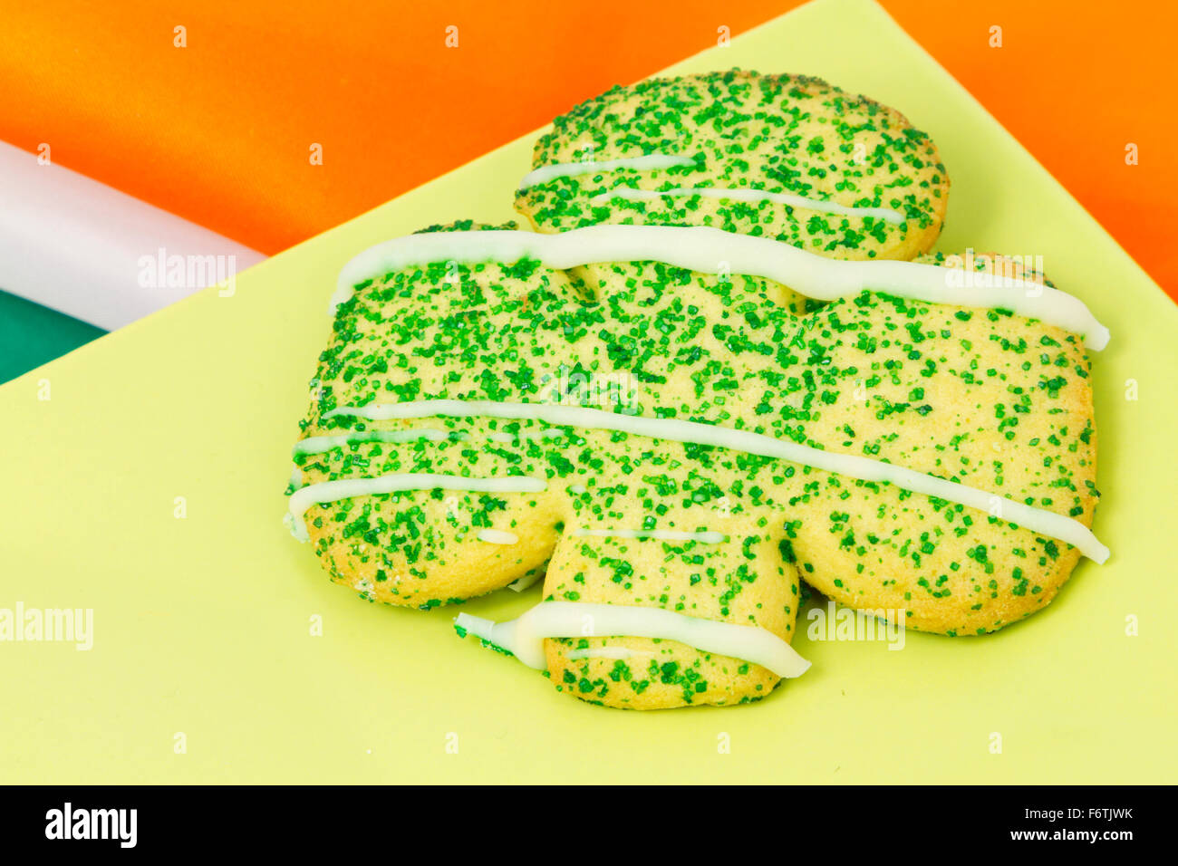 Zucker Cookie schneiden in der St. Patricks Day Kleeblatt Form auf Teller grün mit Orange, weiß und grün Streifen der irischen Flagge als Hintergrund sichtbar. Stockfoto