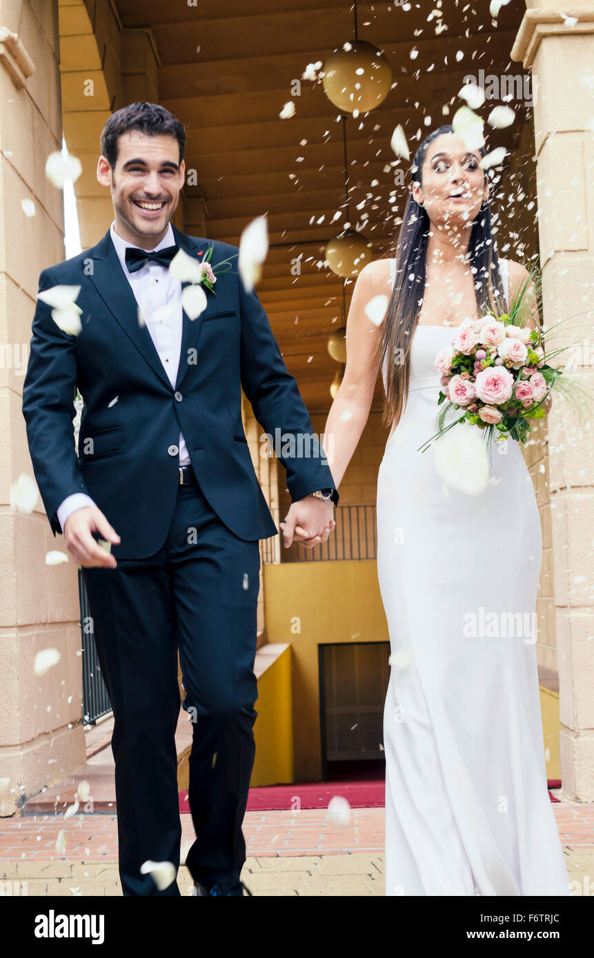 Brautpaar nach der Hochzeit unter Regen aus Rosenblättern und Reiskörner Stockfoto
