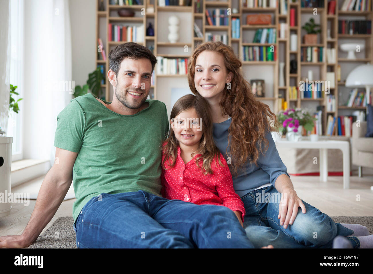 Porträt von kleinen Mädchen und ihren Eltern sitzen zusammen auf Fußboden im Wohnzimmer Stockfoto