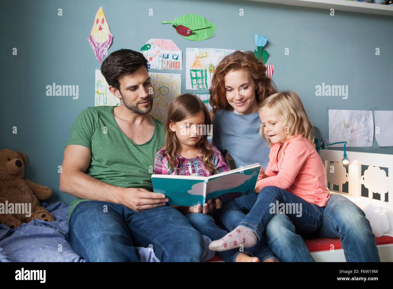 Paar und kleinen Töchter sitzen zusammen auf dem Bett im Kinderzimmer ein Buch zu lesen Stockfoto
