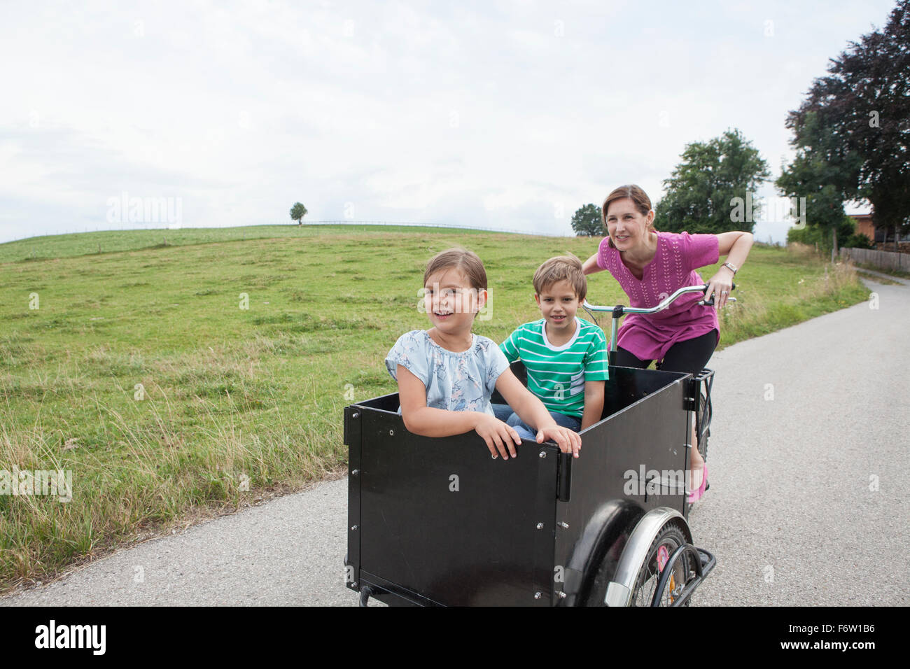Mutter Reiten Fahrrad mit Sohn und Tochter im Anhänger Stockfoto