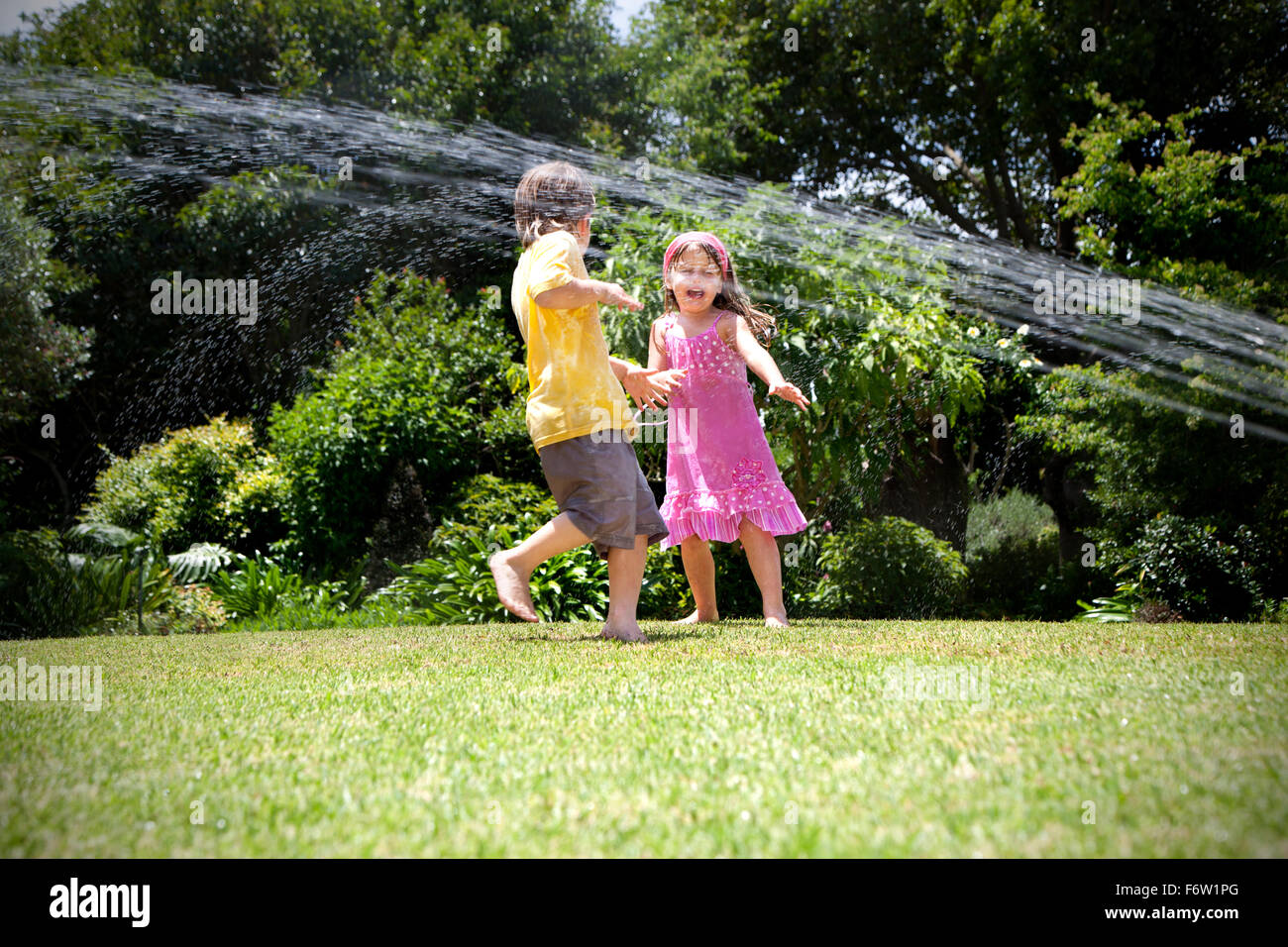Zwei kleine Kinder spielen mit Rasensprenger im Garten Stockfotografie